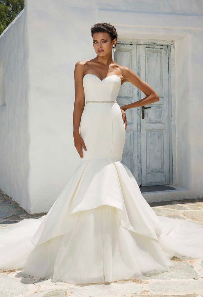 Justin Alexander 8933 is a rich, flawless satin fit and flare gown. The sweetheart neckline creates a feminine top and an embellished belt adds a touch of sparkle. The mermaid fit has an apron skirt of tulle and organza for a dramatic ending.