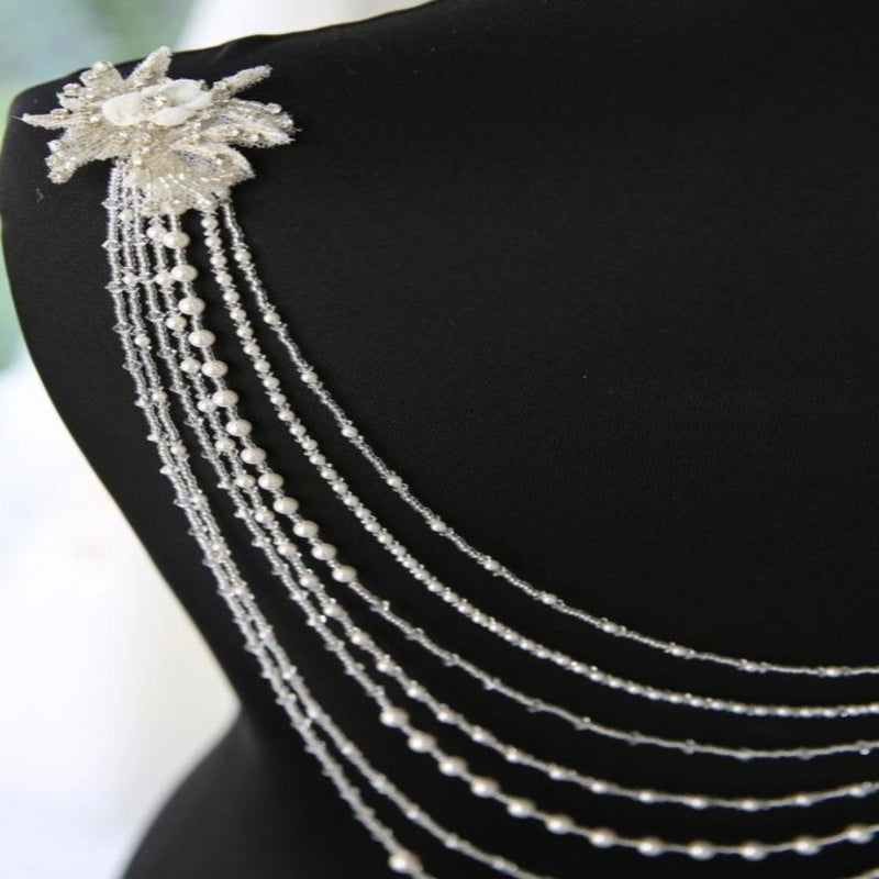 Richard Designs Multi-Strand Dress Jewellery P836 is a seven stranded pearls and crystal back jewellery gathered at the shoulders with hand beaded lace flowers. Simply secure to your gown with the clasps at each end.
