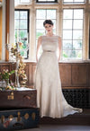 Augusta Jones Ali is an elegant a-line, lace bridal gown featuring all over ivory lace, a camisole sweetheart neckline, illusion back and a satin belt with brooch detail.